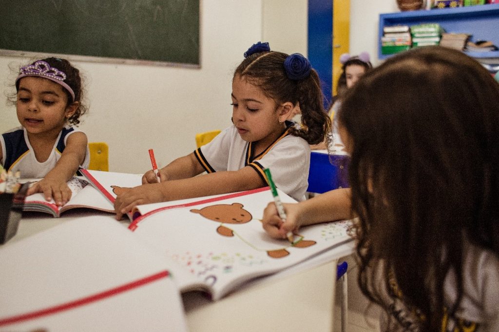 Alunas sentadas colorindo e ampliando seu vocabulário infantil.