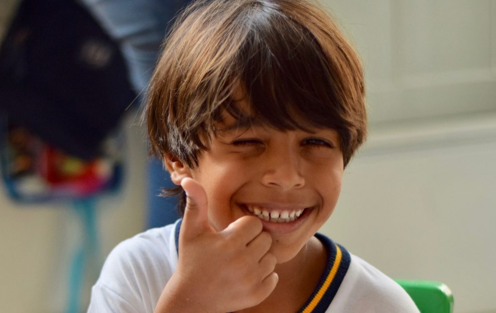 menino sorrindo e fazendo "joinha"