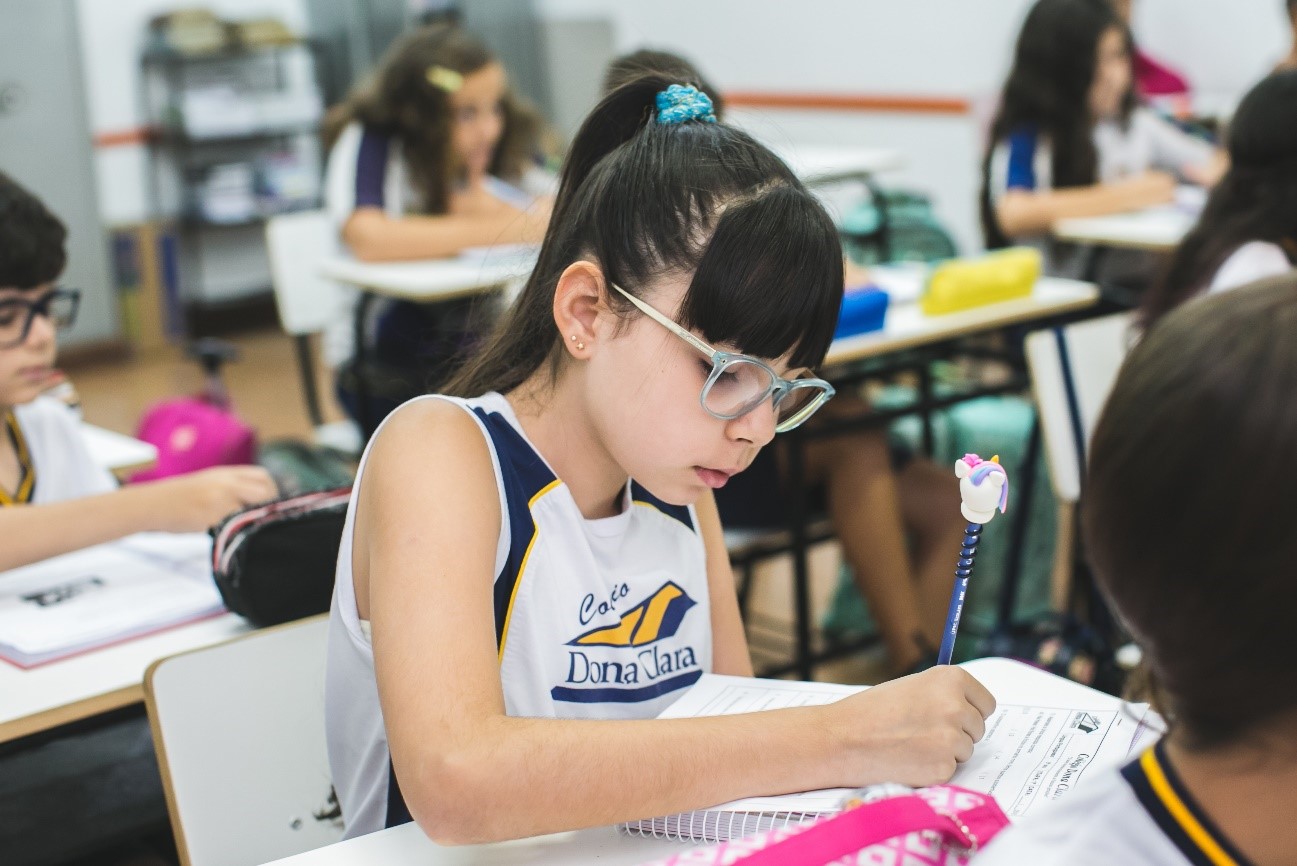 Aluna sentada em carteira em sala de aula ampliando seu vocabulário infantil